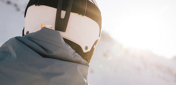 A man is seen from behind wearing a ski helmet, with snow-covered mountains in the background.