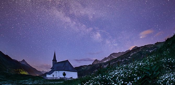 Die Simmelkapelle steht in stiller Nacht, über ihr spannt sich die leuchtende Milchstraße.