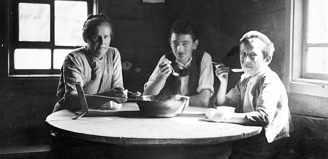 Old photo of three people sitting together at a table and eating.