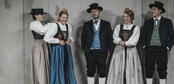 Ladies and gentlemen in Walser traditional costume pose in front of a concrete wall.