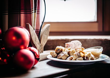 Ein Teller mit Kaiserschmarrn und einer Schale Beilage steht auf einem Holztisch neben roten Weihnachtskugeln.