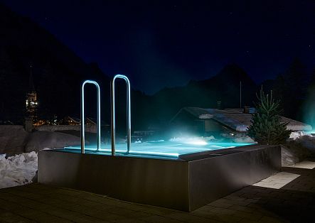 Ein beleuchteter Infinity-Pool im Außenbereich bei Nacht mit Blick auf eine verschneite Bergkulisse.