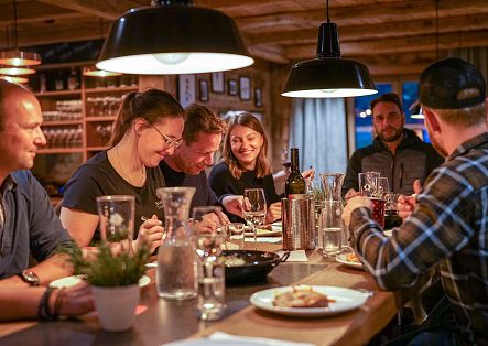 Eine gesellige Gruppe von Menschen, die gemeinsam an einem Holztisch im Restaurant sitzen und essen.