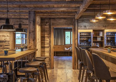 Ein gemütlicher, moderner Gastraum im alpinen Holzdesign mit einer Bar, Hochstühlen und warmer Beleuchtung.