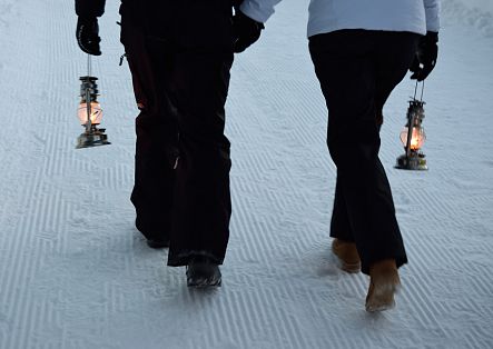 Zwei Personen gehen mit Laternen durch den frisch präparierten Schnee.
