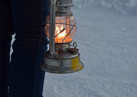 Nahaufnahme einer brennenden Laterne, die von einer Person durch den Schnee getragen wird.