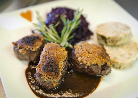 Ein ansprechend angerichtetes Fleischgericht mit dunkler Soße, Rotkohl und Beilagen auf einem weißen Teller.