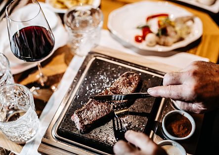 Ein Mann schneidet an einem Tisch ein Stück Fleisch auf einem heißen Stein.