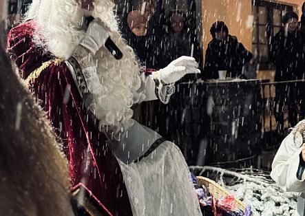 Der heilige Nikolaus spricht in ein Mikrofon und verteilt dabei Geschenke an die Kinder.