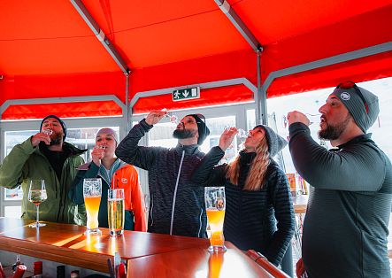 Fünf Personen stehen unter einem roten Dach an einem Tisch und trinken gemeinsam.