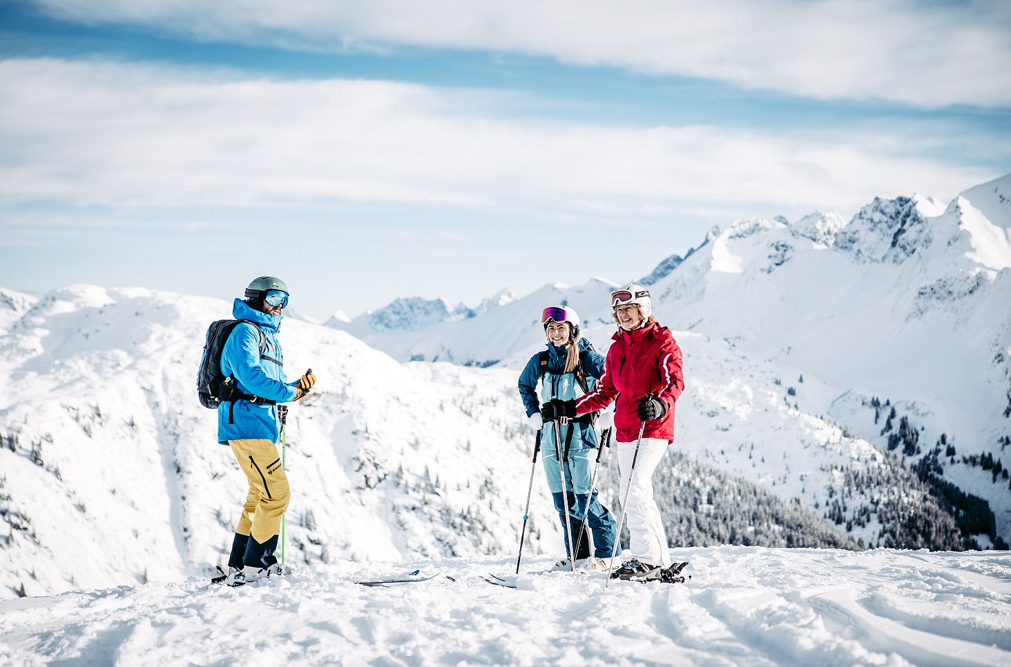 Zwei Personen stehen mit einem Skiguide auf der Piste, während der Guide ihnen die richtige Technik erklärt.