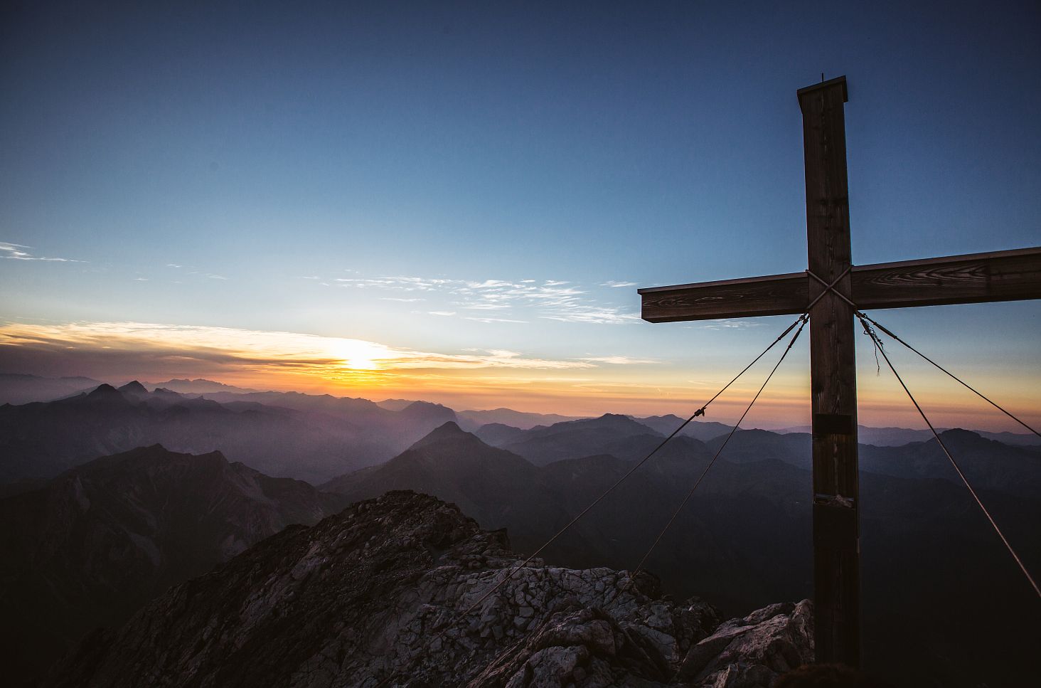 The sun rises behind the Widderstein summit cross, bathing the mountains in golden light.