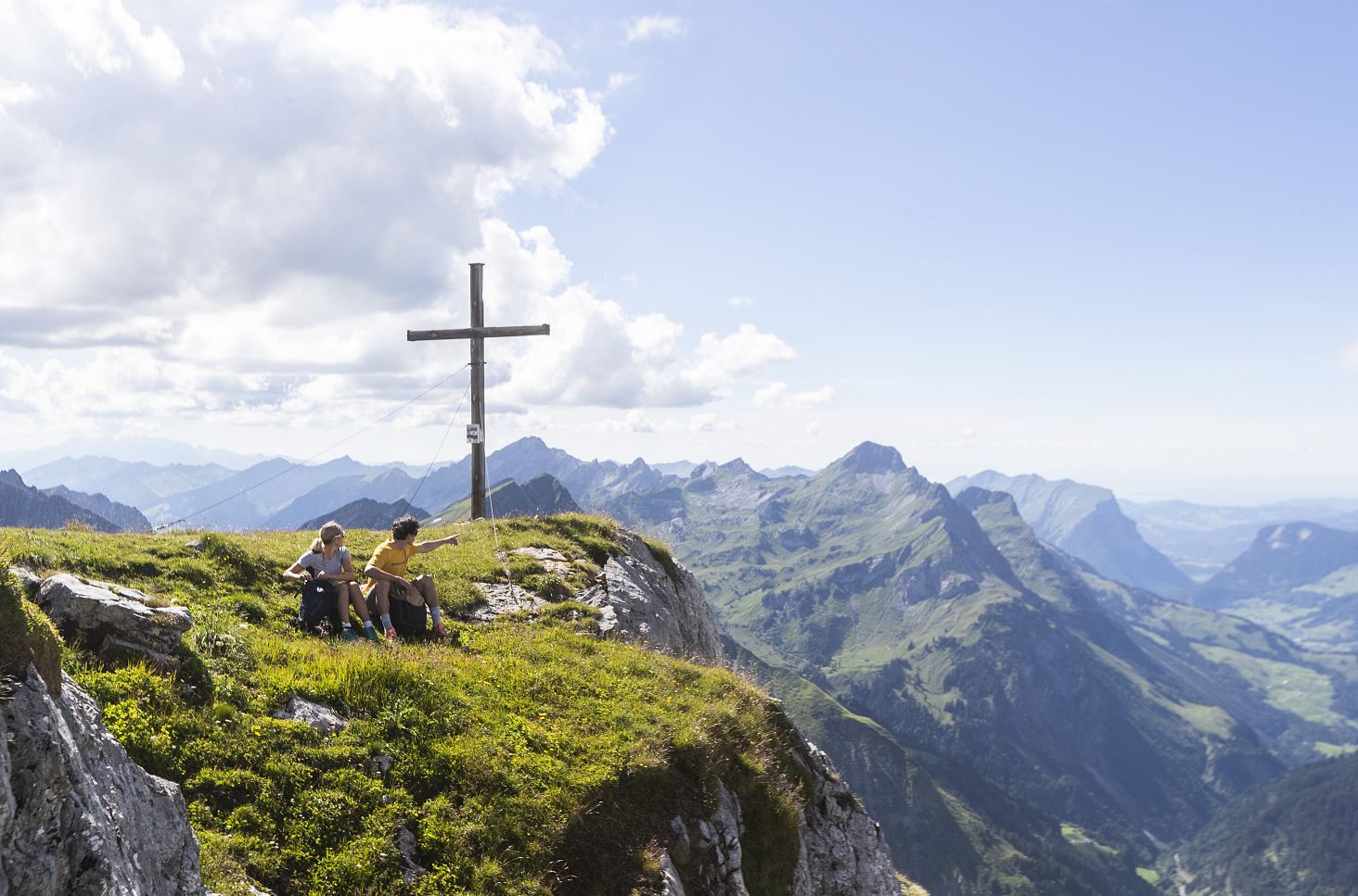 Two people are sitting at the summit of Juppenspitze, enjoying the vast mountain landscape around them.