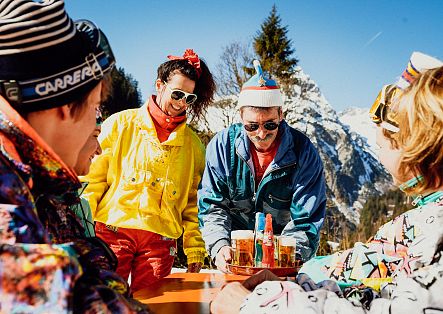 Mehrere Personen stehen an einem Tisch im Schnee und bedienen sich an einem Tablett mit Getränken.