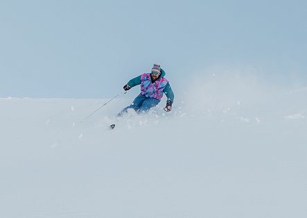 Ein Skifahrer fährt durch tiefen Pulverschnee und ist dabei teilweise von einer Schneewolke umgeben.