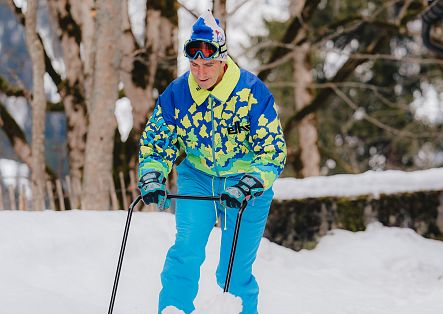 Ein Mann mit Skibrille und Schneehexe steht auf einer verschneiten Fläche vor einem Wald.