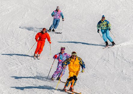 Fünf Skifahrende fahren in unterschiedlichen Abständen gemeinsam eine verschneite Piste hinunter.