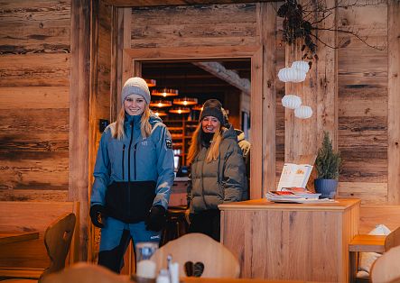Zwei Personen in Winterkleidung stehen am Eingang eines rustikalen Berggasthauses.