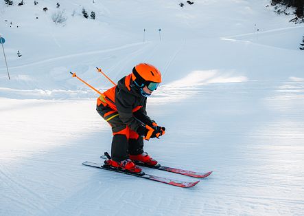 A skier in a dark suit with orange accents is skiing down a snow-covered slope, fully focused.
