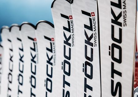 Nahaufnahme mehrerer weißer Stockli-Ski mit schwarzer Beschriftung „STÖCKLI“ und roten Schweizerkreuzen.