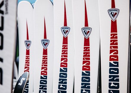 Nahaufnahme mehrerer weißer Ski mit roten und blauen grafischen Markierungen und Logos.