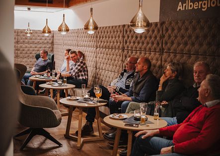 Eine Gruppe von Gästen sitzt an kleinen Tischen in einem stilvoll eingerichteten Restaurant und schaut nach vorne.