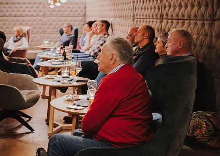 Mehrere Gäste sitzen in gemütlichen Sesseln an Tischen und verfolgen gemeinsam eine Veranstaltung im Restaurant.