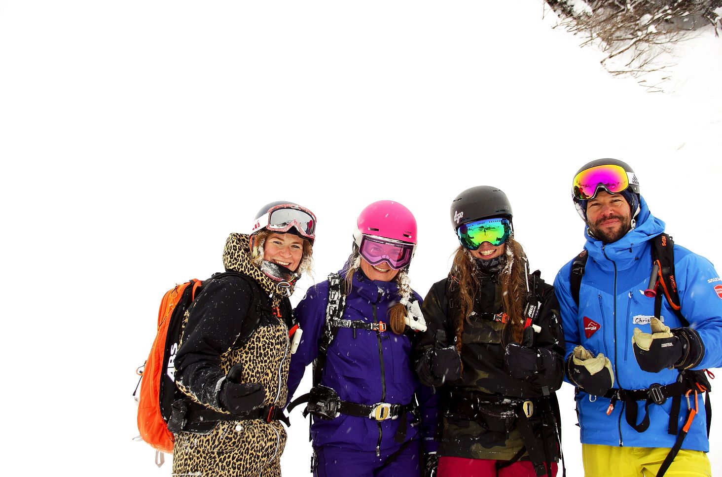 Drei junge Frauen stehen gemeinsam mit ihrem Guide Christian Fritz tief im Powder und lächeln.