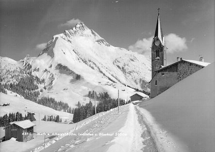 Historic photo of the church in Warth with the Biberkopf in the background, in front of it only a narrow path through the snow.
