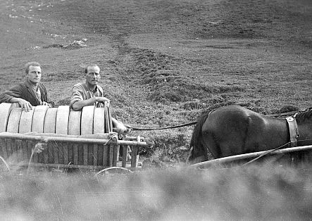 Two men are pulling a horse-drawn trailer full of cheese.