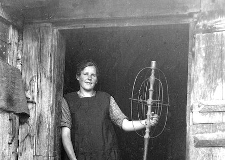 Historic photo of a woman leaning against a wall, holding a device in her hand.