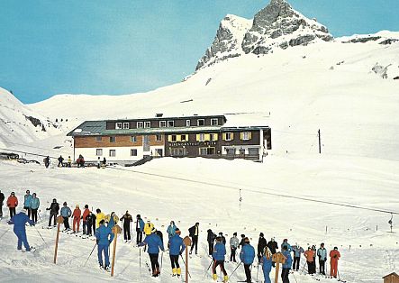 Historic image of the Hotel Alder in winter, with a few skiers in front.