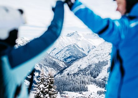 Zwei Personen geben sich ein Highfive, vor ihnen erstreckt sich die verschneite Berglandschaft.