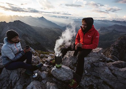 At the summit of Widderstein, two people make themselves a hot coffee and enjoy the view.