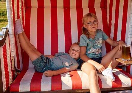 Two children are sitting in a red and white beach chair.