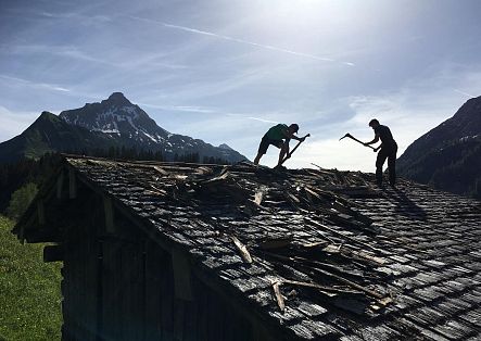 Johannes Strolz helps tear down the roof of an old barn, with the distinctive Biberkopf visible in the background.