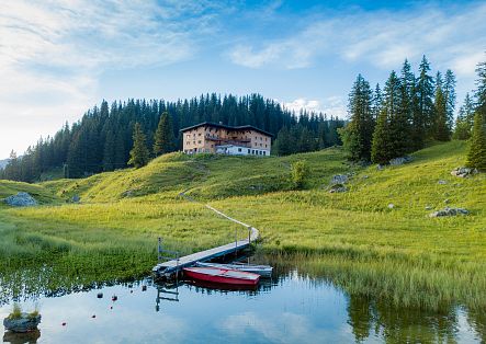 Der idyllische Bergsee Körbersee mit einem kleinen Steg und Ruderboot, umgeben von grünen Wiesen und einem Berghotel im Hintergrund.
