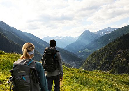 A hiking couple stands high above the valley, enjoying the breathtaking view of the imposing mountain peaks.