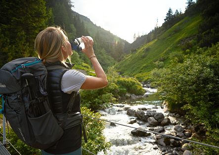 A hiker refreshes herself in a babbling mountain stream, surrounded by lush greenery and wild nature.