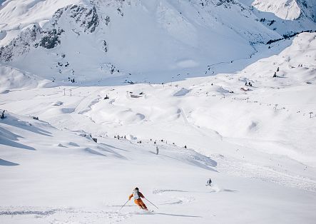 Two people are skiing down a scenic spring snow slope in the sunshine.