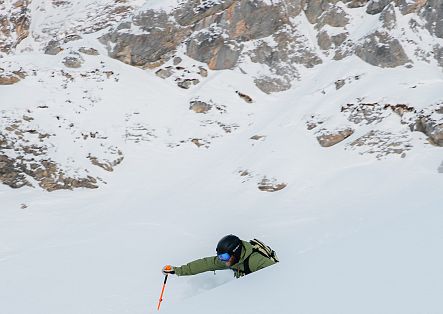 A man in a green ski suit is skiing through deep powder snow.