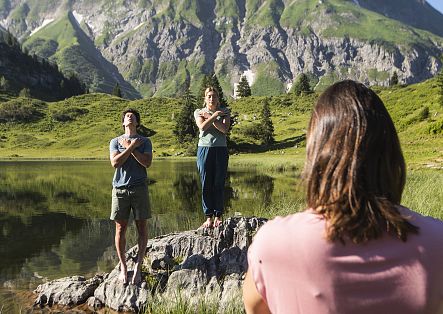 A mindfulness instructor is demonstrating exercises at Körbersee, whilst a couple follow along.