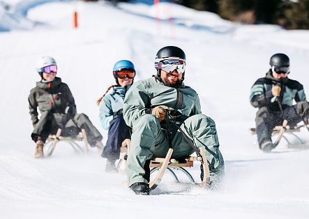 On the Dorfbahn toboggan run, a group enjoys themselves as the sun bathes the scene in warm light.