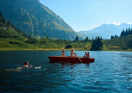Eine Familie ist mit einem Ruderboot auf dem Körbersee unterwegs, während der Vater im Wasser schwimmt.