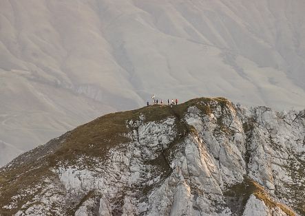 A group of hikers stands on a rocky summit, surrounded by an impressive mountain landscape.
