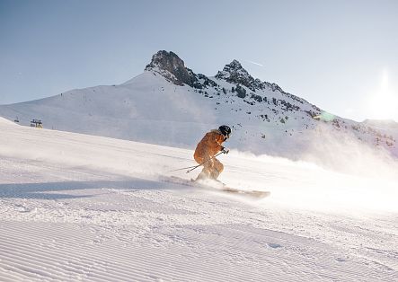 Eine Skifahrerin gleitet Richtung Auenfeld hinab, von der Sonne im Gesicht begleitet.