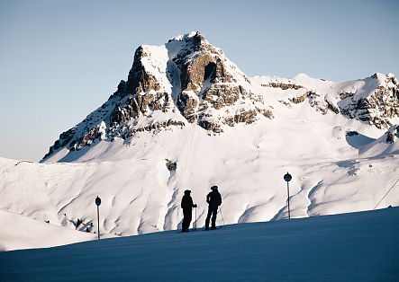 In den frühen Morgenstunden verweilen zwei Skifahrer und richten ihren Blick auf den majestätischen Widderstein.