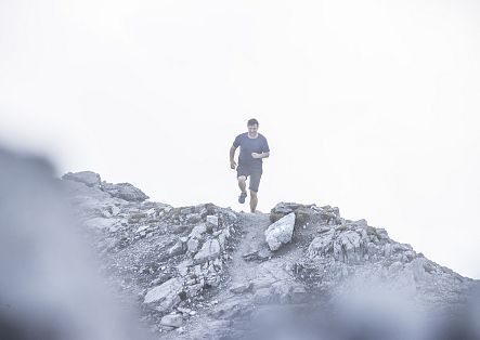 Ein Läufer bewegt sich dynamisch über einen felsigen Grat, umgeben von einer mystischen, nebelverhangenen Atmosphäre.