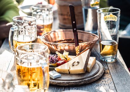 Close-up of a cheese platter in a mountain hut, with a few drinks arranged around it.