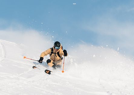 Ein Skifahrer fährt durch tiefen Pulverschnee und wirbelt dabei Schnee auf.